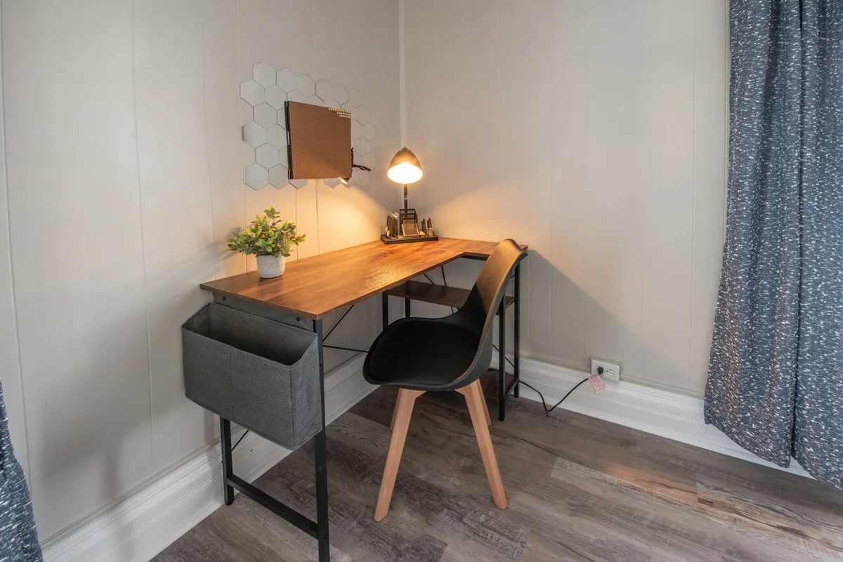 A calm interior with a functional desk setup, accented by a lamp, mirror, and a small plant. The space combines practicality with style, offering a glimpse of integrated storage and workspace that would appeal to guests seeking everyday functionality.