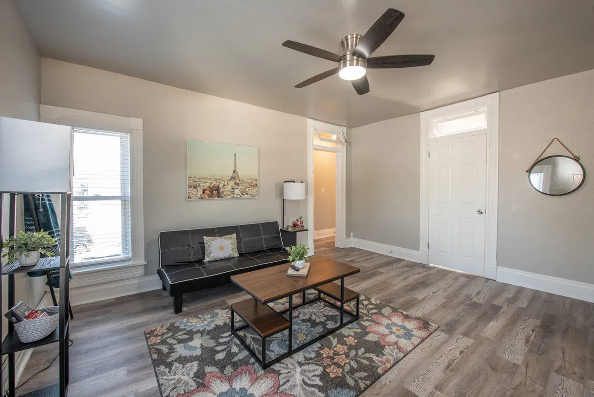 A stylish living room scene shows a comfortable sofa, a wooden coffee table, tasteful wall art, and a textured rug. The space feels inviting and is well-suited for both quiet afternoons with a book or lively gatherings with friends. The overall vibe is cozy and entertainment-ready, matching the room's intended use.