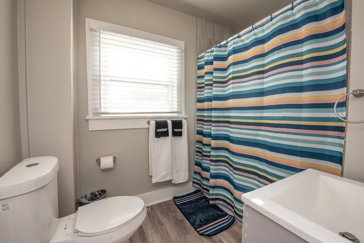 This image features a contemporary bathroom with a striped shower curtain, plush white towels, a modern toilet, and a soft bath mat. The space is brightly lit and exudes a fresh, inviting atmosphere, ideal for daily routines.